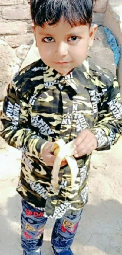 Adorable boy in a camouflage shirt holding a banana.