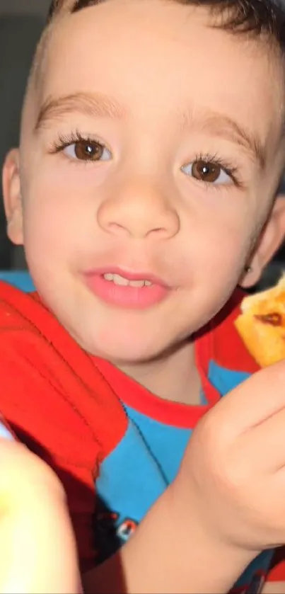 Child smiling and holding a snack with vibrant colors in a close-up shot.