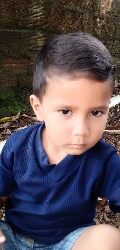 Cute child sitting outdoors with a navy blue shirt in a natural setting.