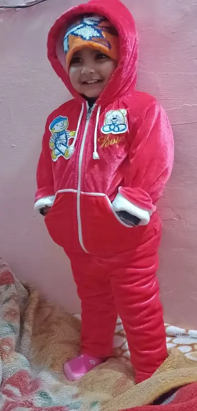 Smiling child in red winter outfit with pink background.