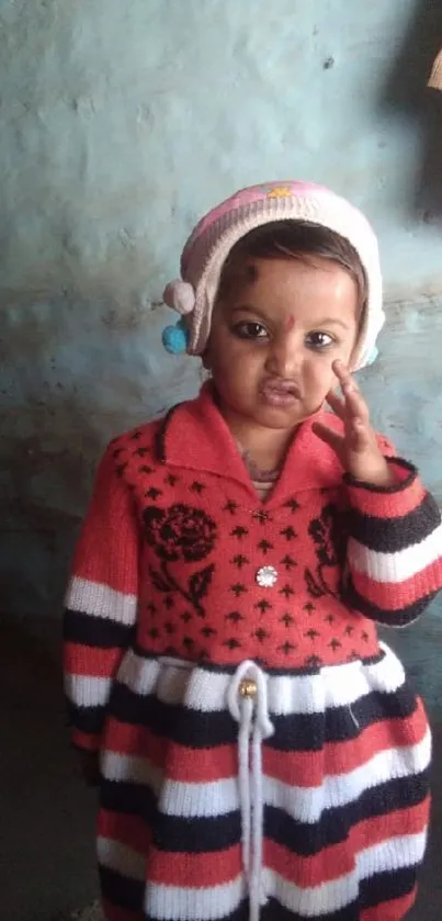 Cute child in a striped winter outfit against a blue wall.