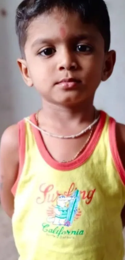 Young child wearing a yellow shirt with red accents.