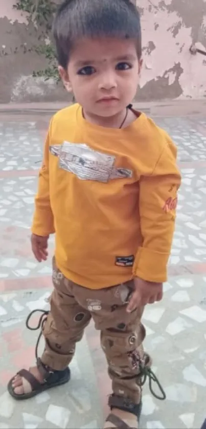 Cute child in yellow shirt standing on a tiled floor.