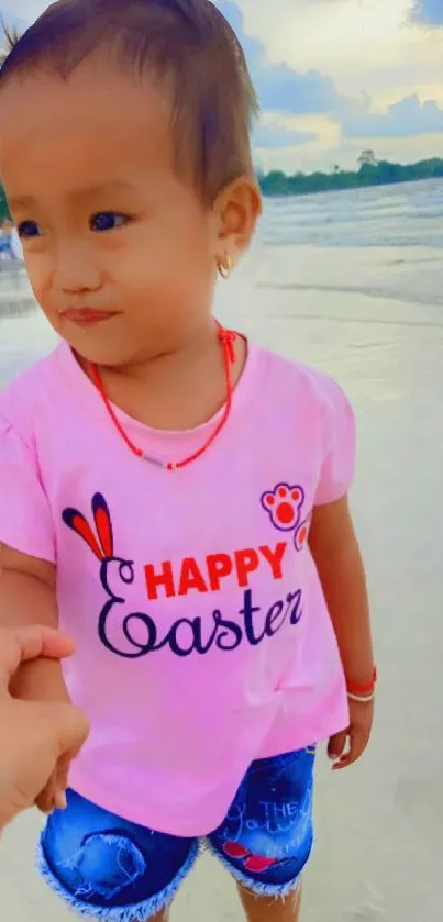 Child in pink shirt holding hands on the beach.