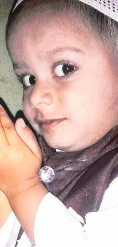 Cute child with hands in prayer wearing a white cap and brown outfit.