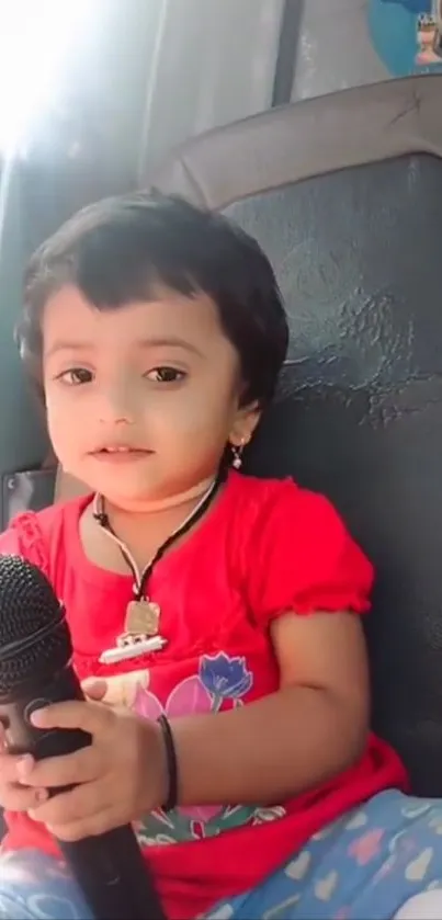 Cute child holding a microphone in a red dress.