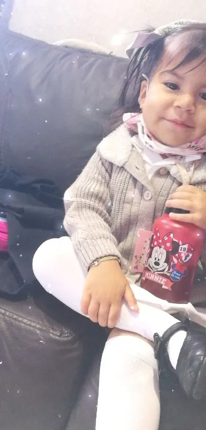 Child with Minnie Mouse bottle on sofa.