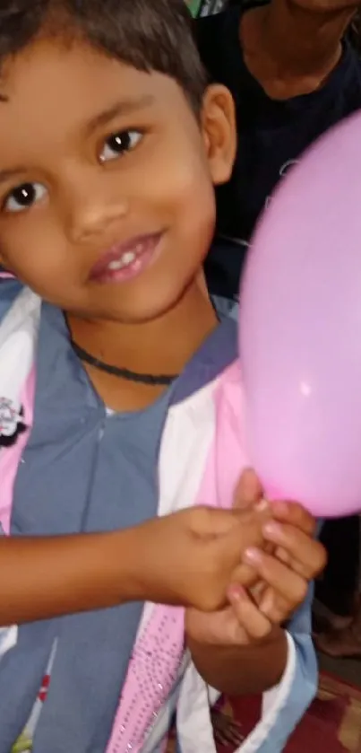 A smiling child holding a pink balloon, creating a joyful scene.