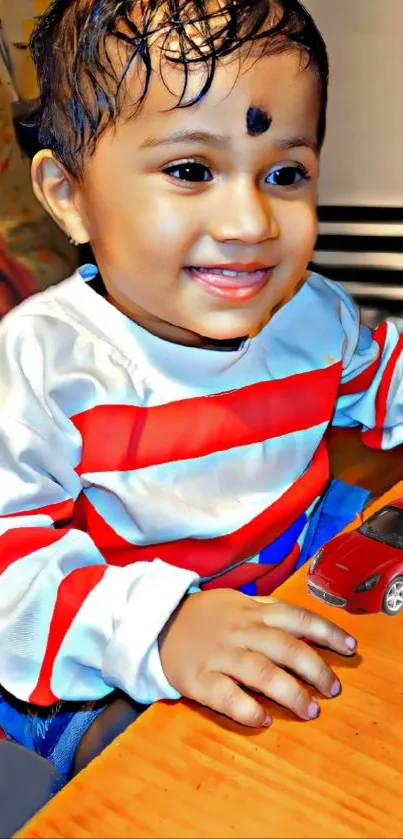 Smiling child with a toy car on a table, wearing a striped shirt.