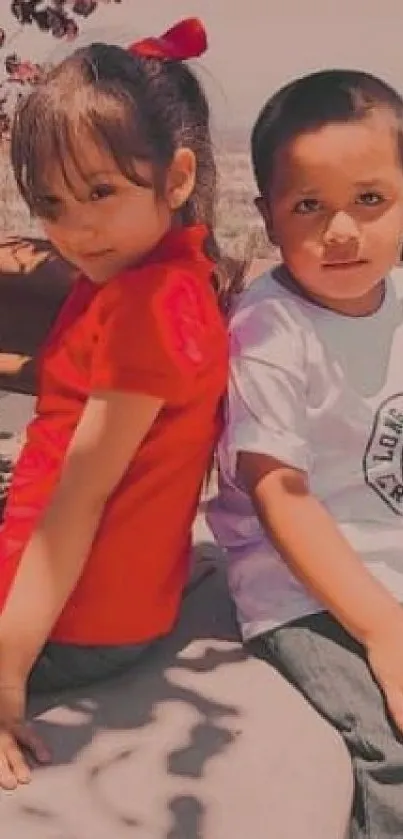 Two children sitting outdoors, one in red.