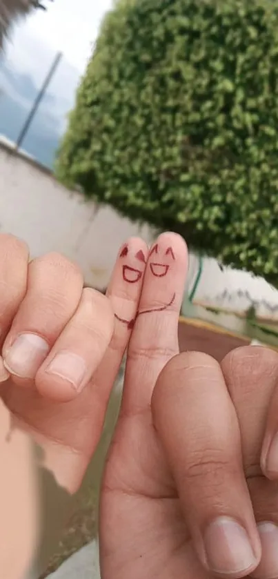 Cute smiling faces drawn on fingers against a leafy green background.