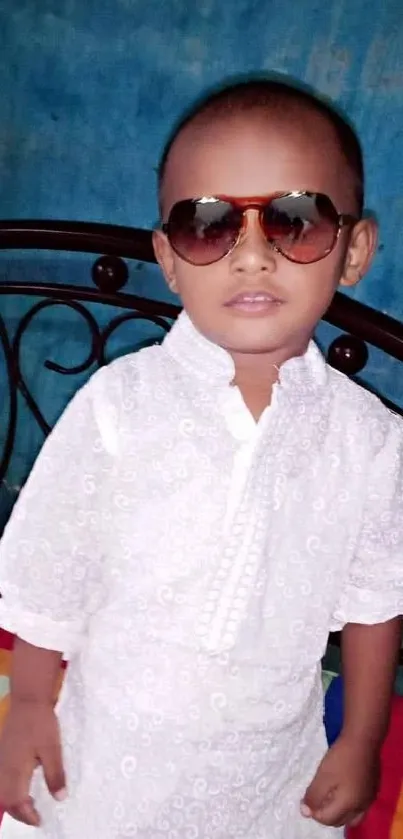 Cute child wearing sunglasses and white attire in a vibrant setting.