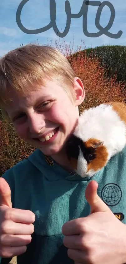 Smiling child with a guinea pig on his shoulder outdoors.