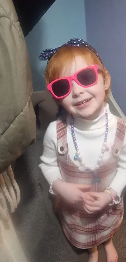 Child in plaid dress and pink sunglasses.