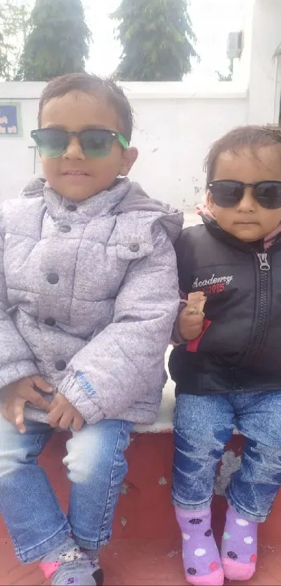 Two kids in stylish winter outfits sitting outside.