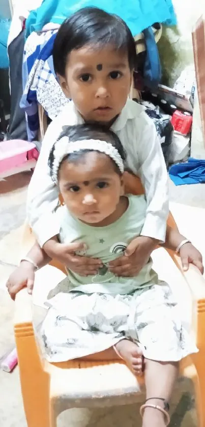 Two children sitting on a chair with playful expressions.