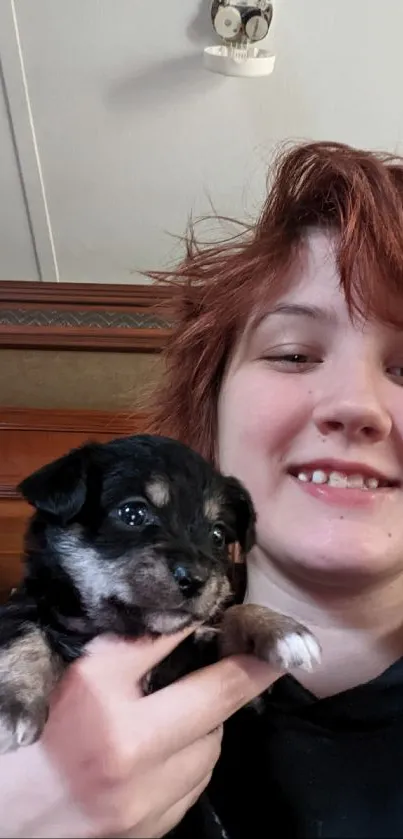 Girl smiling while holding a cute puppy indoors.