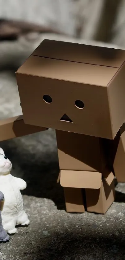 Adorable cardboard robot with two toy cats on a stone surface.