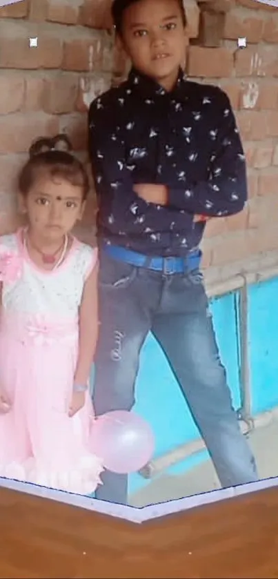 Children posing with a pink balloon against a brick wall.