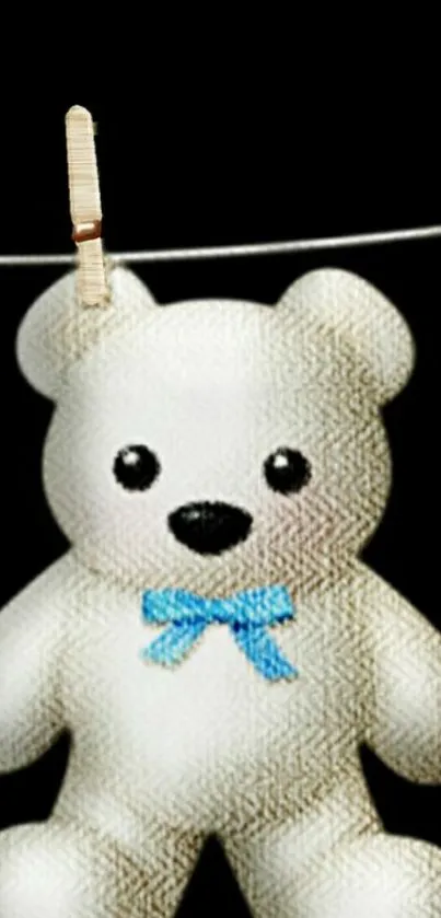 Cute teddy bear with blue bow hanging on a line against black background.