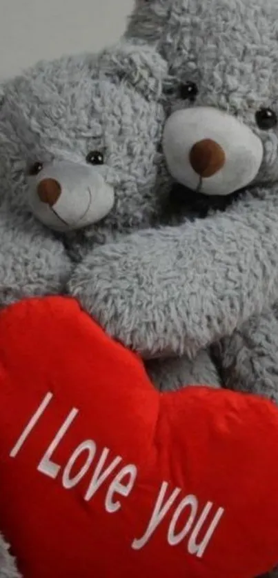 Two grey teddy bears hug a red heart pillow with 'I Love You' text.