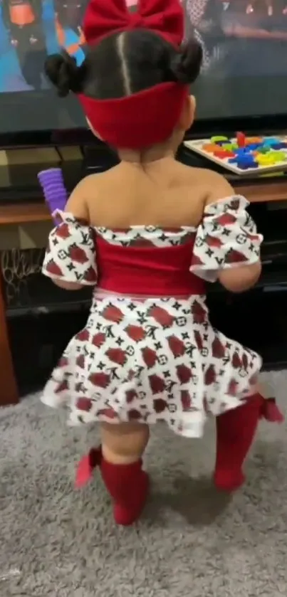 Charming toddler in red and white dress standing on a gray carpet.