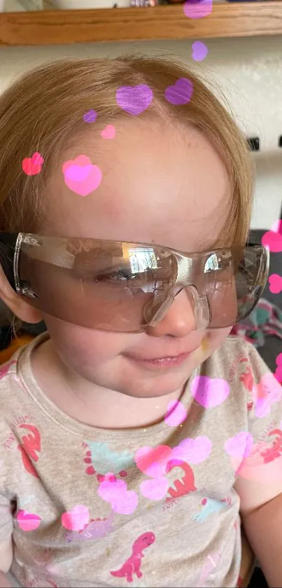 Adorable toddler smiling, wearing large glasses in a cozy home setting.