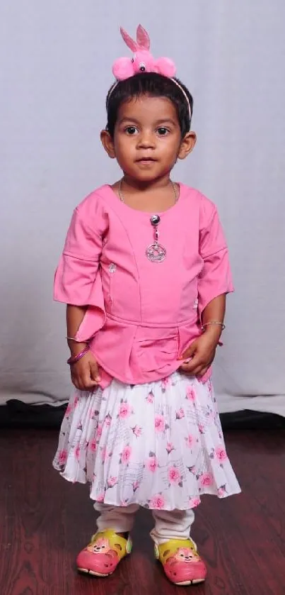 Cute toddler in pink outfit with floral skirt on wooden floor.