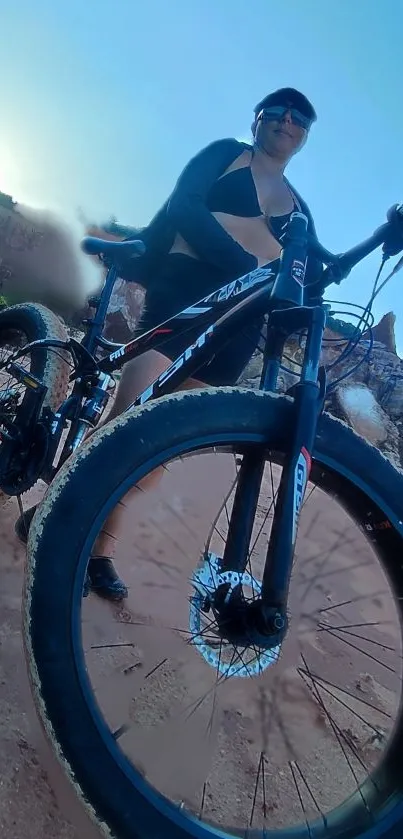 Cyclist on mountain trail with blue sky background.