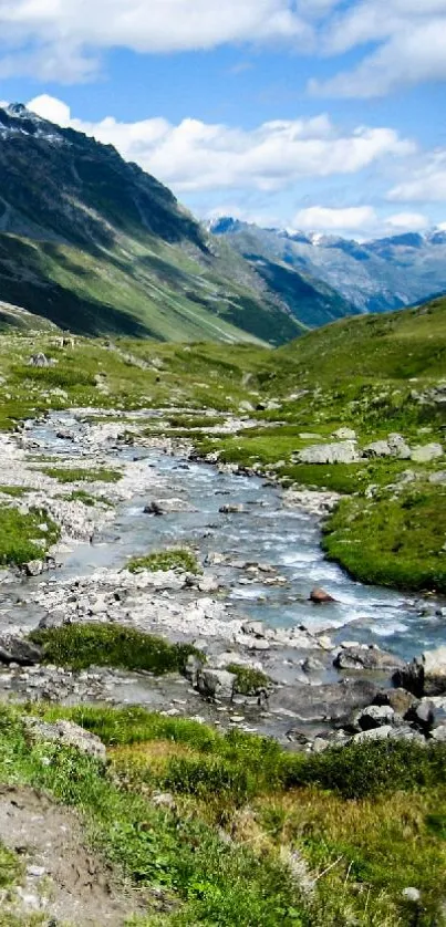 Cyclists travel through a green mountain valley beside a river under a blue sky.