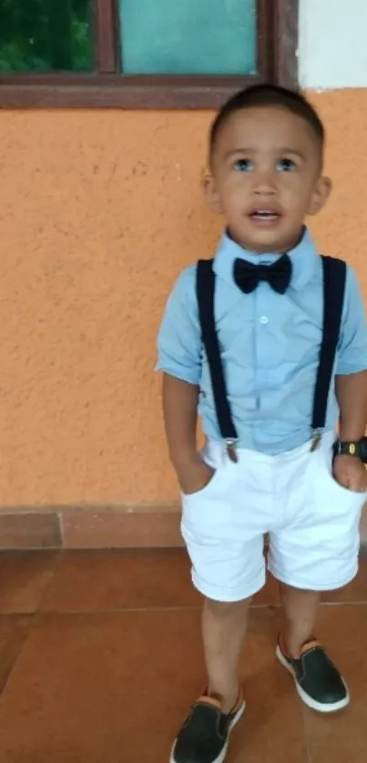 Child in blue shirt, white shorts, with orange wall.