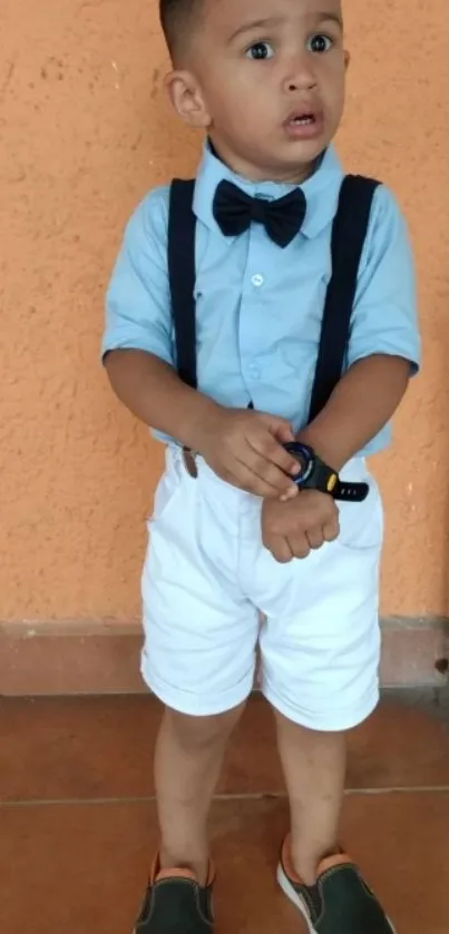 Young boy in blue shirt and bow tie standing stylishly.