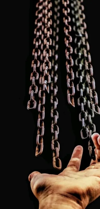 A hand reaching towards hanging chains on a dark background.