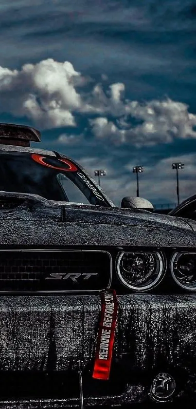 Dark muscle car under dramatic cloudy night sky.