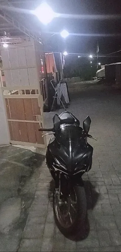 A sleek black motorcycle parked under streetlights at night on a paved urban street.