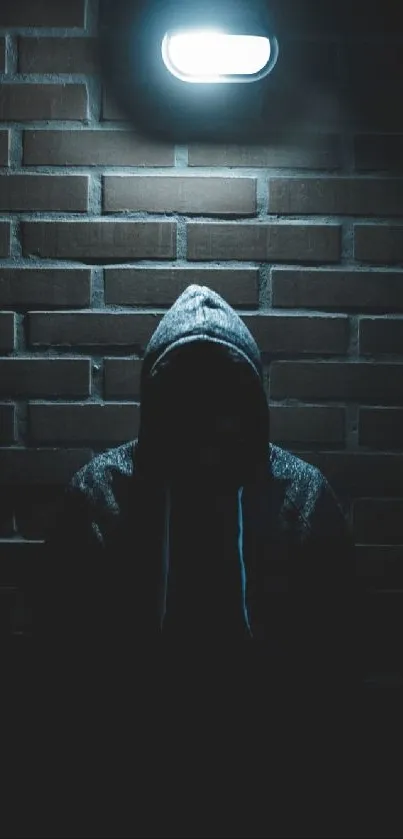 Dark silhouette in hoodie under a bright streetlight against a brick wall.