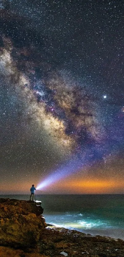 Person shining light at a star-filled night sky over the ocean, revealing the Milky Way.