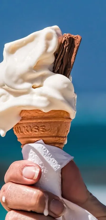 Hand holding ice cream cone with blue sky background.