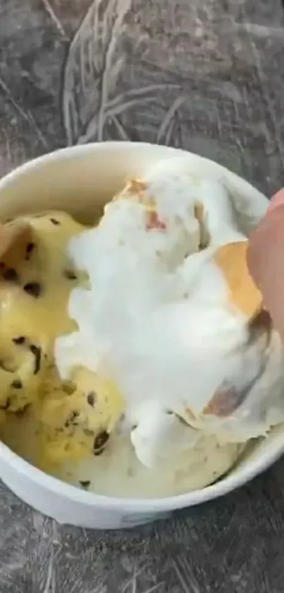 A cup of chocolate chip and vanilla ice cream on a rustic table.