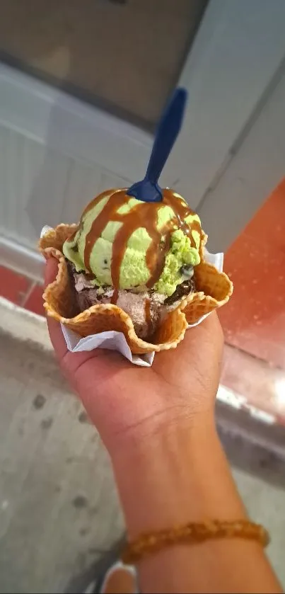 Hand holding an ice cream cone with chocolate syrup and green ice cream.