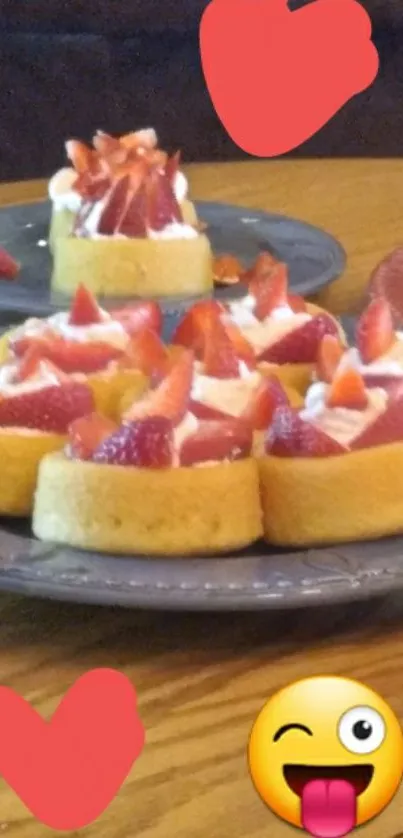 Strawberry-topped cakes on a wooden table with hearts and emoji.