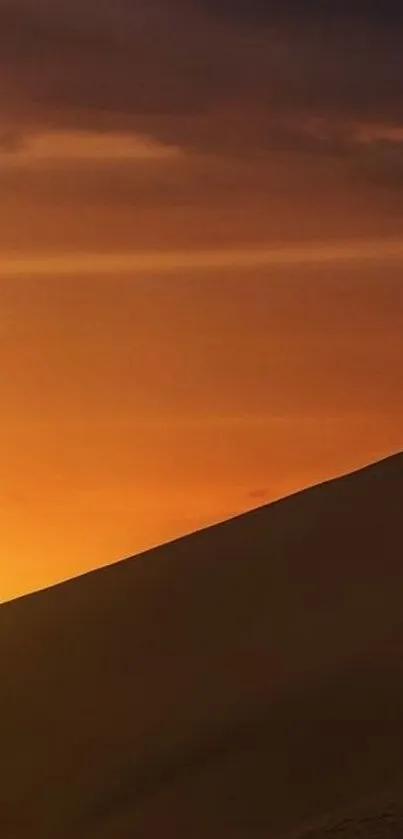 Desert sunset with dune silhouette and orange sky.