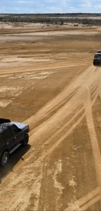 Two vehicles on a sandy desert road under clear blue skies.