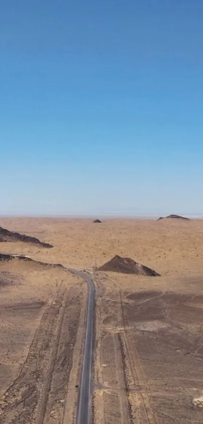 A lonely road stretches through a vast desert under a clear blue sky.