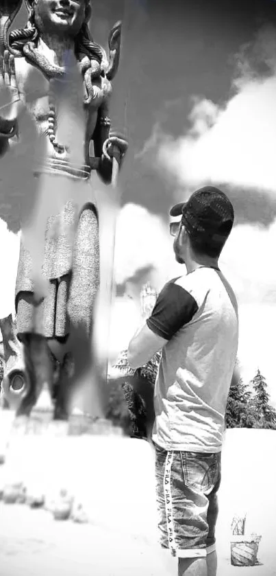 Monochrome image of man praying before a large statue outdoors.