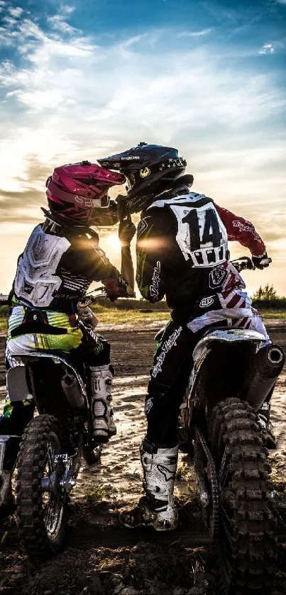 Two motocross riders pause at sunset on a dirt track.