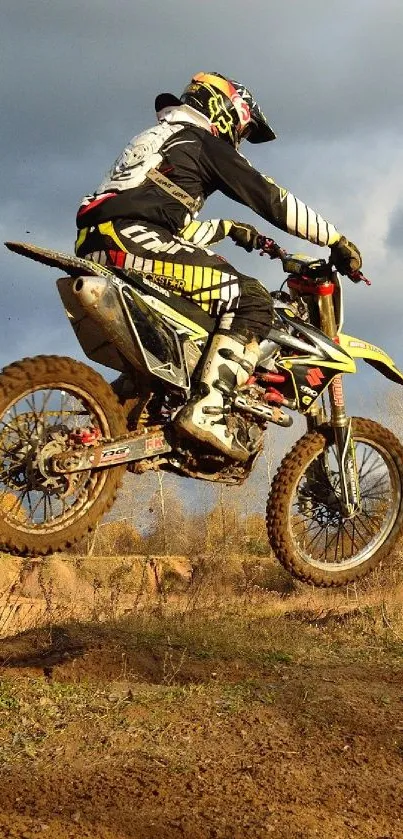 Dirt biker catching air on a motocross track against a cloudy sky.