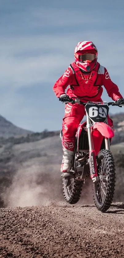 Red motocross rider on dirt track with mountain backdrop.