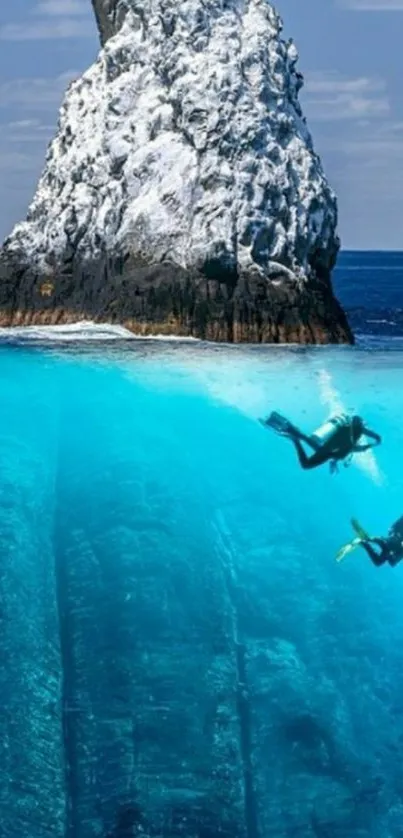 Two divers explore rocky underwater scene with towering ocean rock.