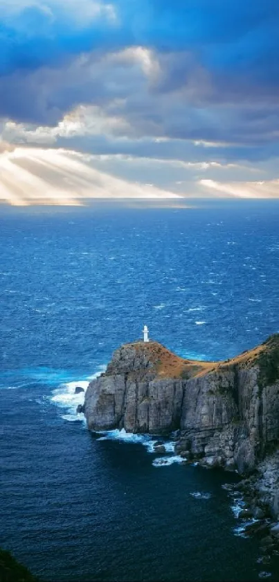 Lighthouse on a cliff with vibrant blue ocean and dramatic cloudy sky with sunbeams.